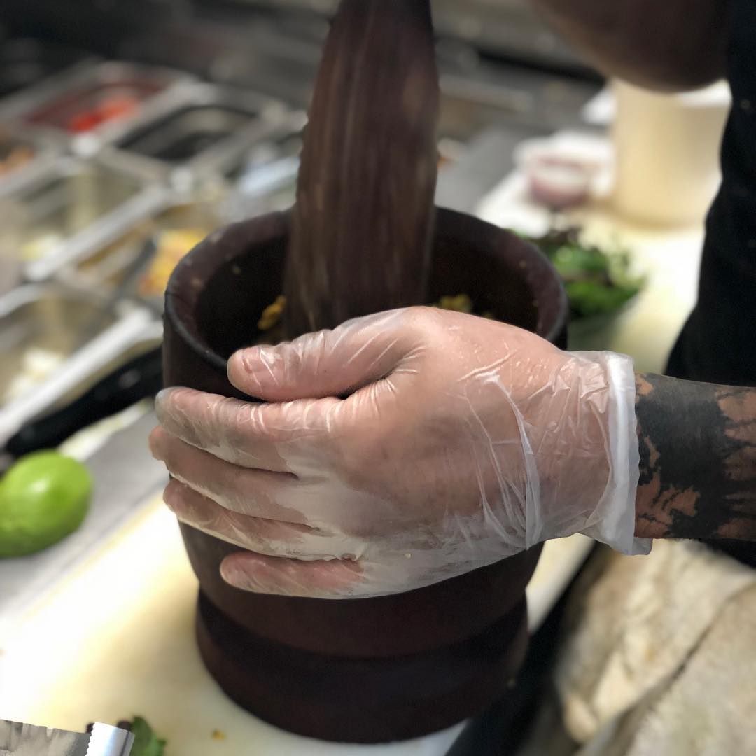 Gloved hands mashing mofongo in a wooden pilón in the Kokí kitchen