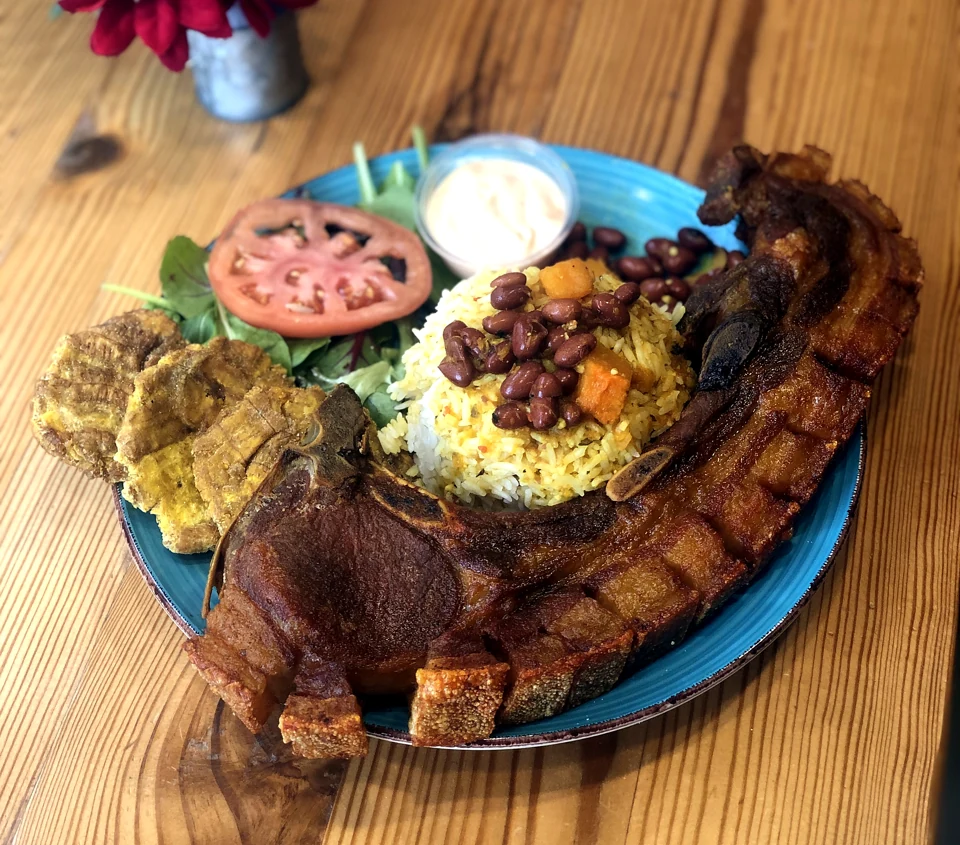 Kokí can-can pork chop with rice, beans, tostones, and salad on a turquoise plate